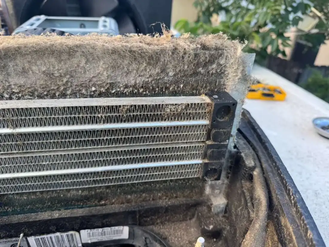 Rooftop RV air conditioner condenser coil packed solid with grass and debris with the unit open on the roof