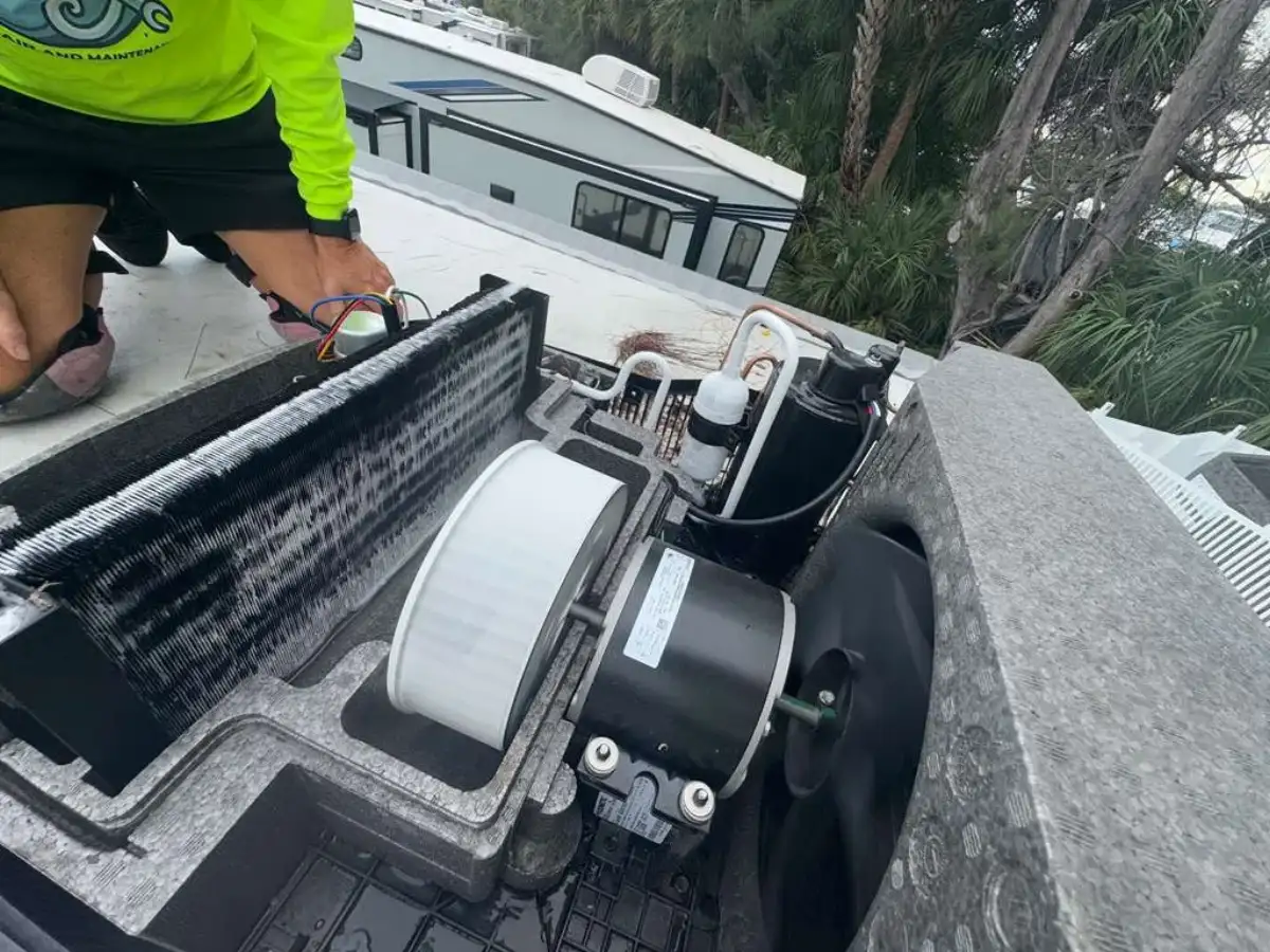 Technician working inside an opened rooftop RV air conditioner with other RVs and palms in the background