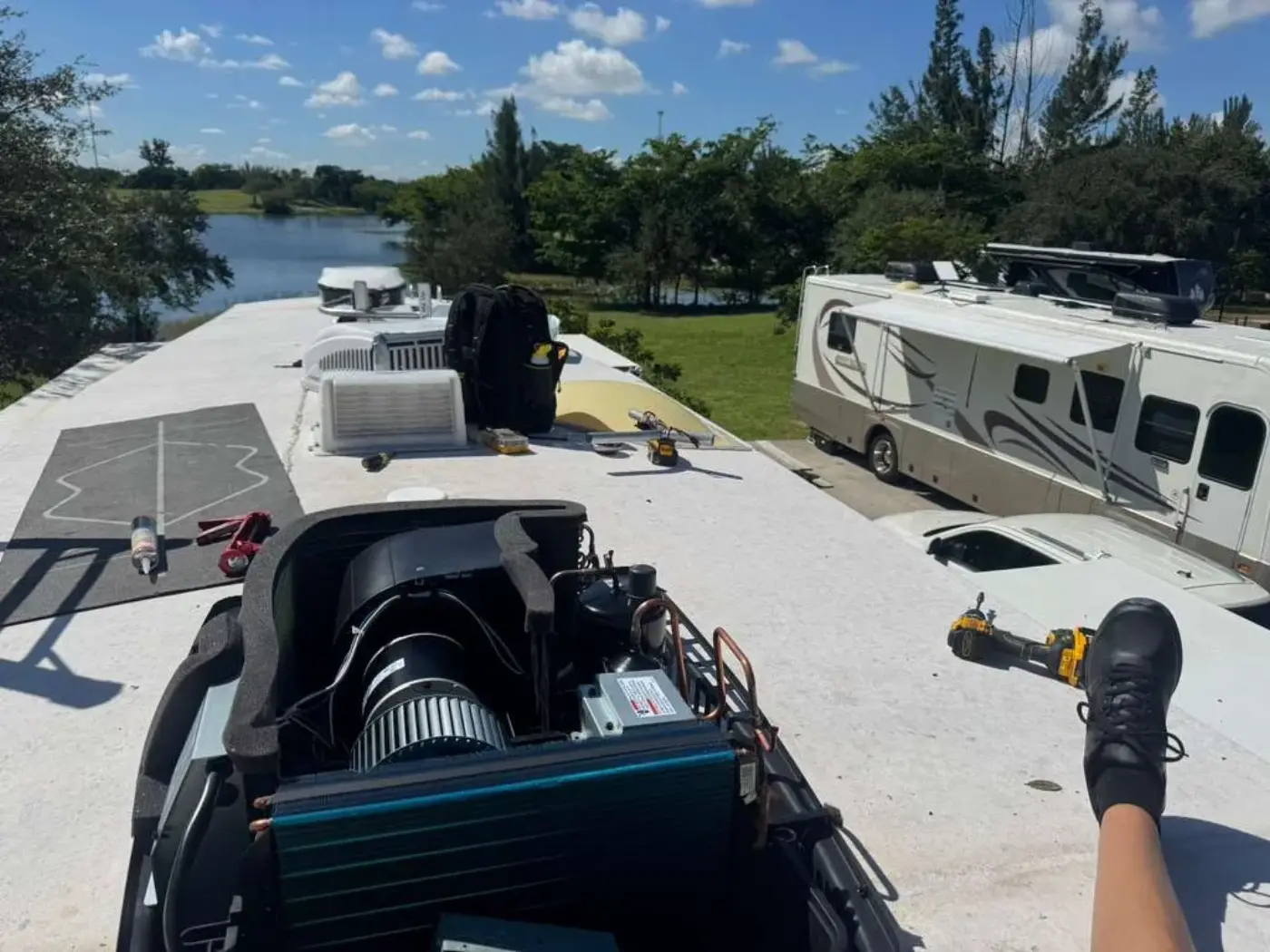 Rooftop air conditioner opened up on an RV roof at a lakeside Florida park with other motorhomes behind