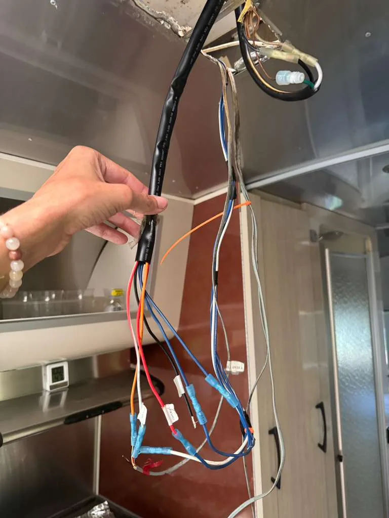 Hand holding a wiring harness inside an opened RV cabinet above the galley
