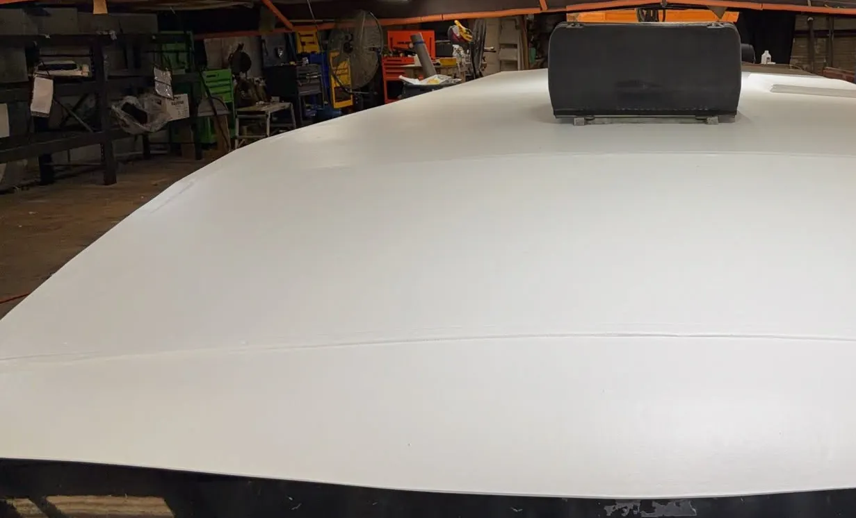 New white TPO membrane fitted over the front cap of an RV inside a workshop